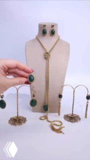 Набор ювелирных изделий Claudio Canzian на белом фоне: длинное колье с зеленым камнем, серьги и браслеты; продавец демонстрирует комплект рукой.