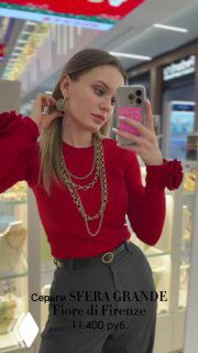 Женщина в красном свитере в магазине примеряет многослойное золотистое колье Fiore di Firenze, видна витрина и интерьер магазина.