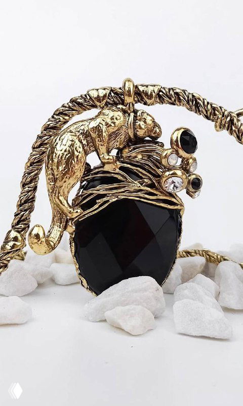 Крупный план кулона Claudio Canzian с чёрным гранёным камнем в окружении золотых декоративных листьев и мелких кристаллов на белых камнях.