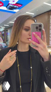 Женщина делает селфи в зеркале бутика; на фото видны украшения на руке, часть торгового зала и образ, демонстрирующий бижутерию бренда.