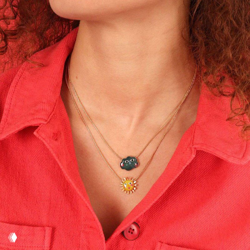 Две тонкие золотистые цепочки TARATATA с маленькими кулонами — солнце и облачко, аккуратно смотрятся на летнем вырезе.