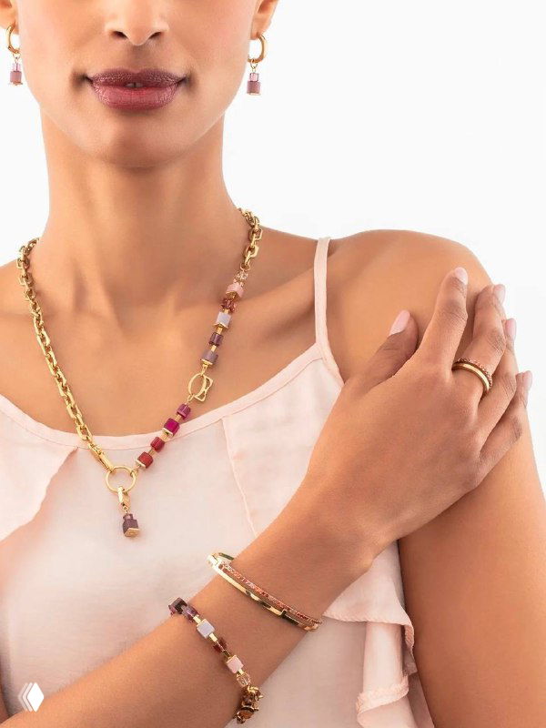 Крупный план модели в светлом топе: золотистая цепочка с цветными вставками и браслеты Coeur de Lion, подчёркивающие оттенки кожи и летний настрой.