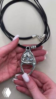 Рука держит треугольный подвес AMARRE с крупными прозрачными кристаллами на черных шнурах, нейтральный фон и вид спереди.