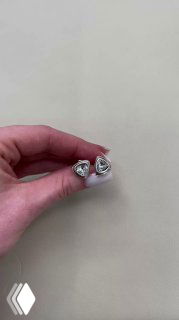 Крупный план: рука показывает пару треугольных сережек AMARRE с прозрачными кристаллами в серебристой оправе на светлом фоне.