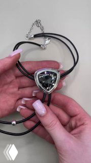 Подвес AMARRE на черных шнурах крупным планом: серебристая оправа и заметный прозрачный кристалл, изделие держит рука с маникюром.