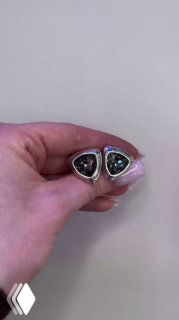 Детальный кадр треугольных сережек AMARRE с прозрачными кристаллами в серебристой оправе, рука держит изделие на однотонном фоне.