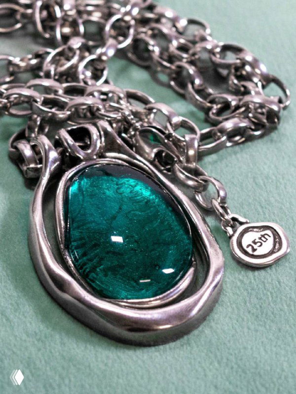 Крупный план металлической подвески Ciclon с глубоким зелёным муранским стеклом на цепочке, видны текстура металла и игра света на вставке