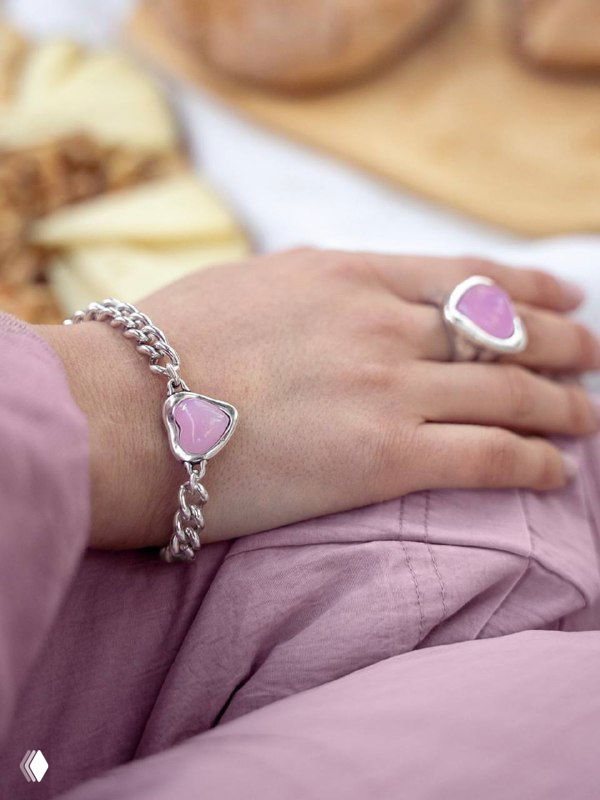 Руки в спокойных пастельных тонах держат браслет и кольцо Ciclon с нежно‑розовой муранской вставкой, показ текстуры металла и формы