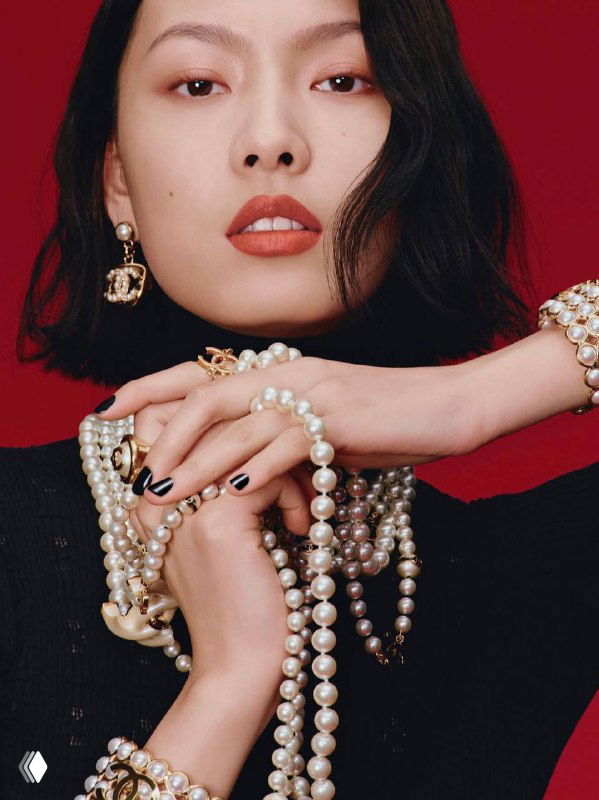 Портрет женщины с крупными жемчужными украшениями и серьгами на красном фоне — рекламный образ с акцентом на аксессуары.