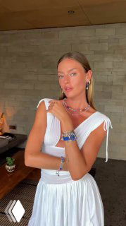 Модель в белом платье демонстрирует разноцветные украшения Coeur de Lion — колье, браслеты и серьги; интерьер магазина виден на заднем плане, рекламный контекст.