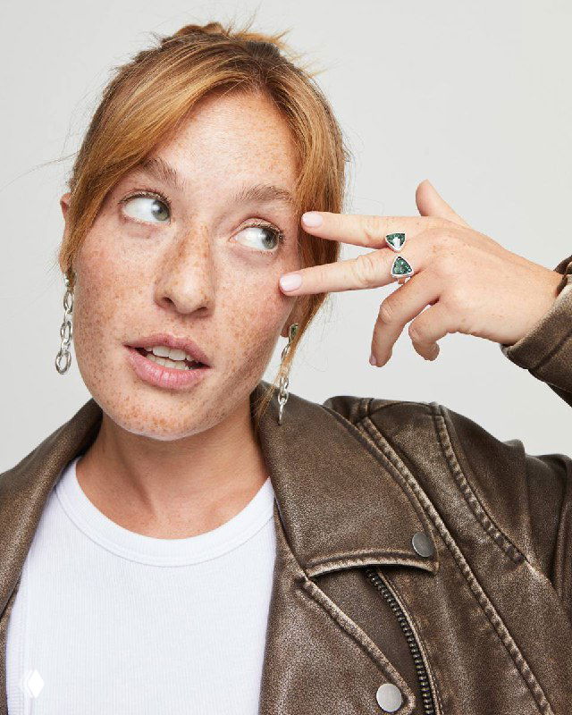 Женский портрет с рукой у лица, видны серьги и кольца из коллекции Ser Camaleonica (UNOde50); фэшн-кадр на светлом фоне.