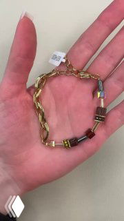 Крупный план: рука держит золотистый браслет с декоративными элементами и биркой, детальное фото самого украшения в ладони.