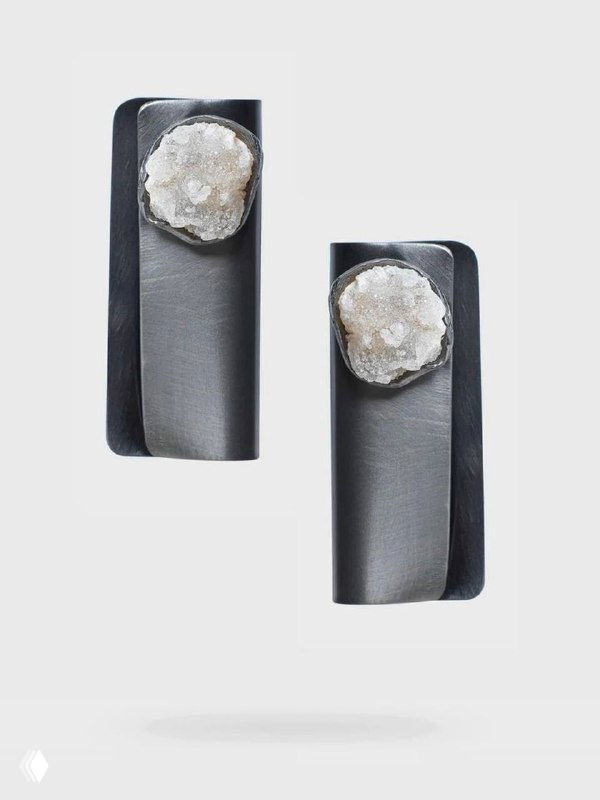 Фото минималистичных серьг KATERINA VASSOU из тёмного металла с текстурной вставкой белого натурального камня на нейтральном фоне, крупный план.