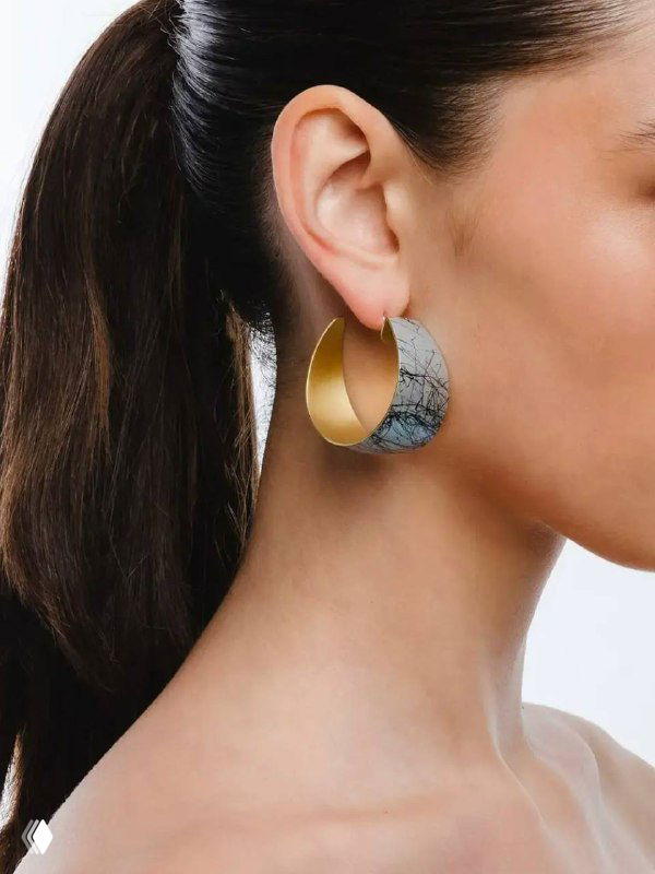 Профиль женщины, в ухе крупная полукруглая серьга KATERINA VASSOU: наружная металлическая поверхность и внутренняя фактура, подчёркнута на светлом фоне.