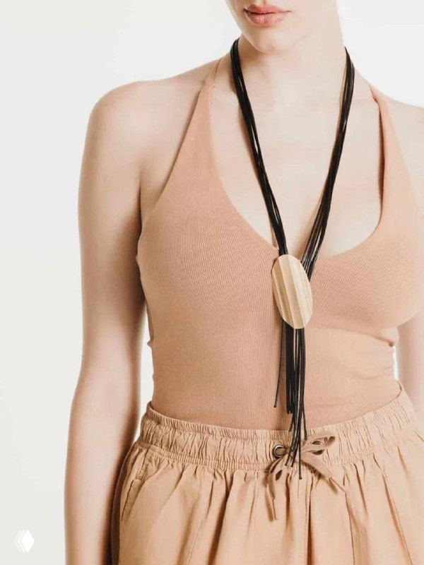 Модель в бежевом топе демонстрирует длинное ожерелье KATERINA VASSOU с подвеской из дерева или металла на кожаном шнуре, подчёркивая кэжуал-стиль аксессуара.