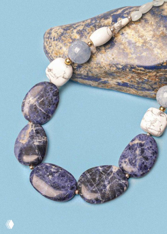 Крупный план бус и камней коллекции Arctique от Nature Bijoux на голубом фоне: овальные синие и кремовые вставки, текстура натурального камня видна.