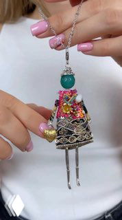 Видео-кадр/фото: держат в руках подвеску-куклу MIAMELIE с ярким текстильным платьем и декоративной отделкой — демонстрация в руках модели.