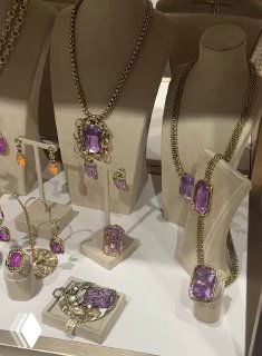 Витрина с крупными аметистовыми камнями в золотых основаниях: ожерелья, кольца и серьги расположены на белых подставках.