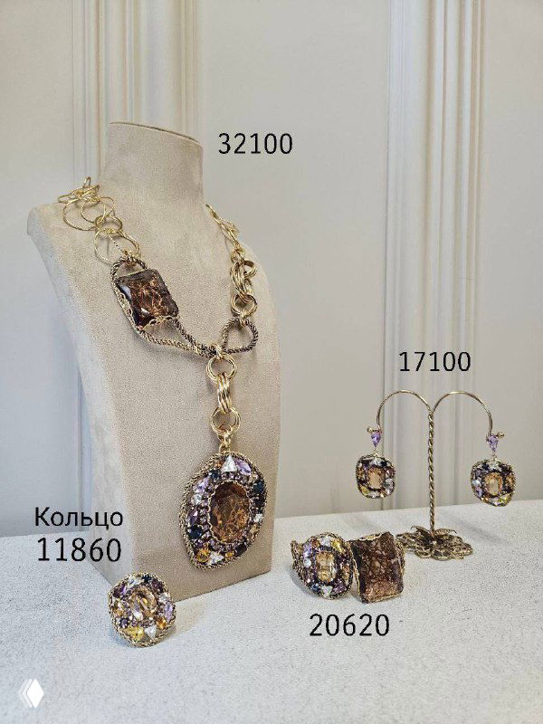 Золотистое ожерелье с большим центральным камнем и набор сопутствующих изделий на манекене; видны ценники и пронумерованные позиции.