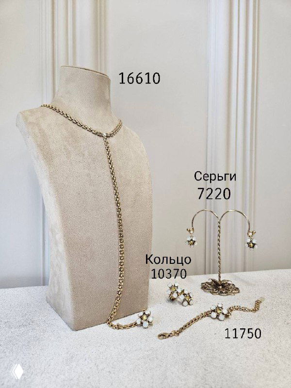 Изящное длинное колье и несколько комплектов украшений с ценами на фоне пастельной витрины — подборка тонких золотистых цепей и колец.