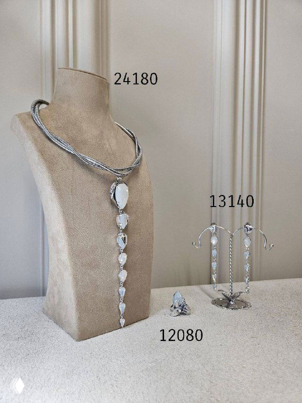 Белое ожерелье с каскадом камней и серьгами на светлом манекене; рядом указаны ценники изделий, оформленные в витрине бутика.