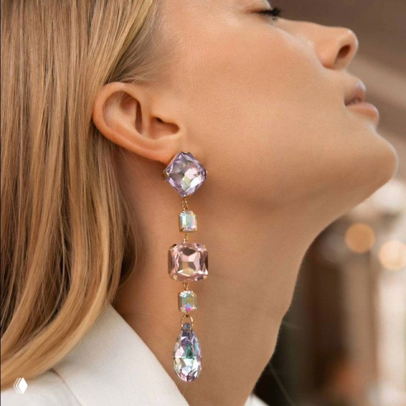 Рекламное фото: модель в профиль в длинной висячей серьге из многофактурных кристаллов и подвесок, демонстрация посадки украшения.