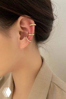 Крупный план на ухо модели с несколькими каффами: изящные серебристые и золотистые кольца в верхней части уха на нейтральном фоне.