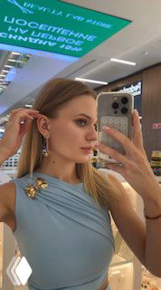 Портретное селфи в бутике: девушка примеряет серьги и показывает боковой профиль вместе с подсветкой витрины и украшениями.