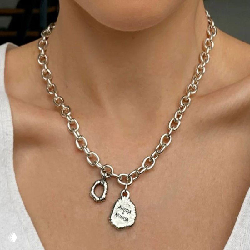 Крупный план серебристого ожерелья-цепочки с подвеской и гравировкой «AHORA O NUNCA», съёмка на шее модели при мягком студийном свете.