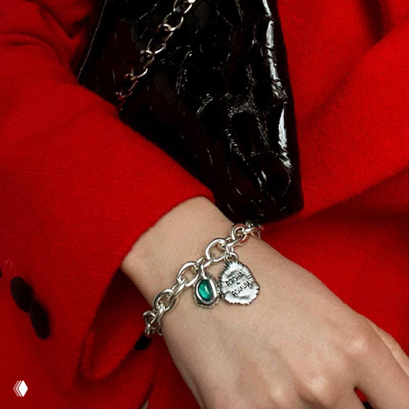 Браслет Ciclon на запястье женщины: серебристая цепочка с бирюзовой муранской вставкой, контраст красного пальто и чёрной сумки в кадре.