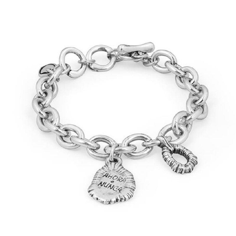 Студийный снимок браслета Ciclon: крупная серебристая цепочка с металлической медалью, на которой видна гравировка «AHORA O NUNCA», чёткая детализация.