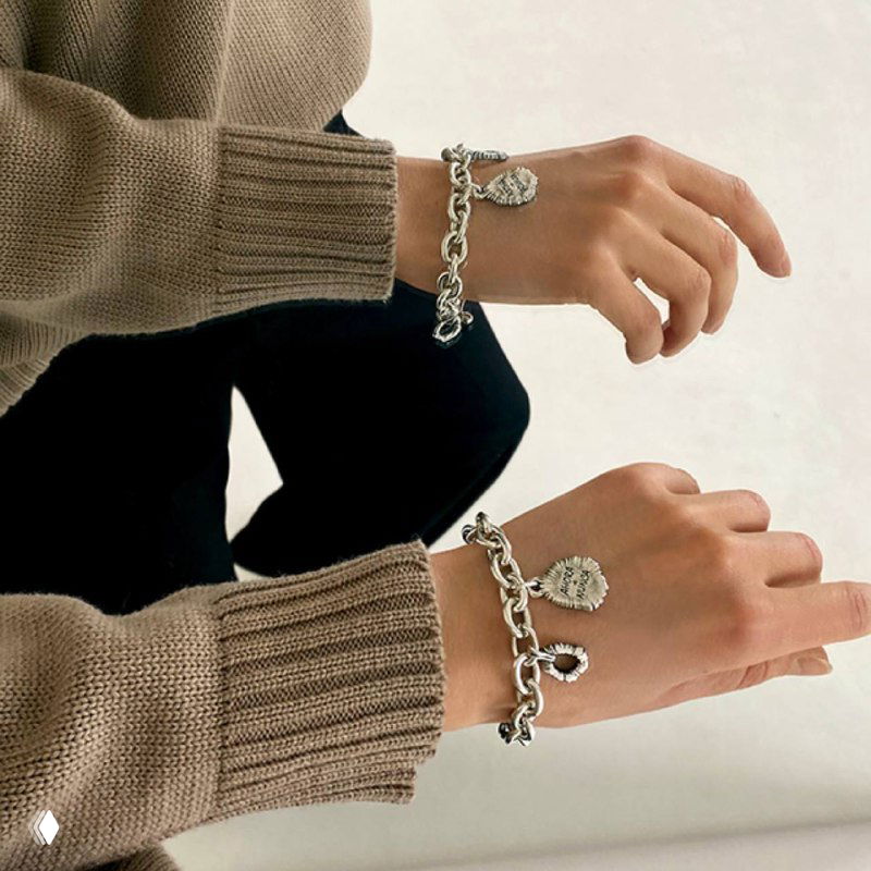 Две руки в бежевых свитерах демонстрируют браслеты Ciclon на запястьях; акцент на звеньях цепи и металлических подвесках в повседневном кадре.