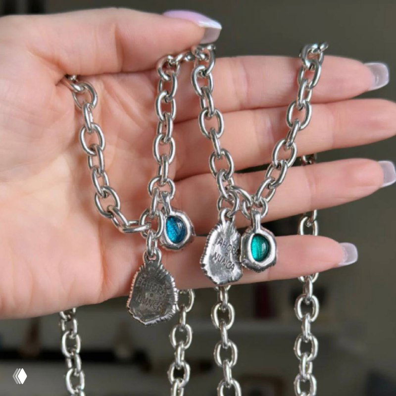 Руки держат несколько ожерелий и браслетов с подвесками «Ahora o Nunca», видны бирюзовые муранские вставки и крупная серебристая цепь для сравнения вариантов.