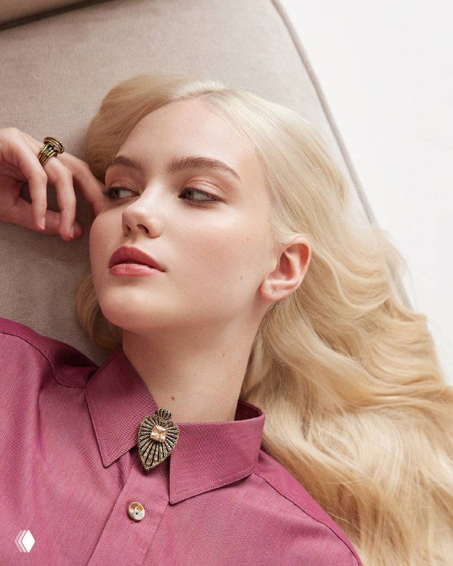 Женская модель в романтическом образе, лежит на диване с закреплённой у воротника брошей‑подвеской Fiore di Firenze, студийный портрет