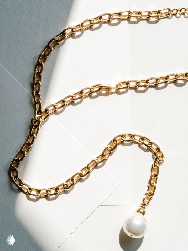 Крупный план золотистой цепи Claudio Canzian с подвеской из крупного белого жемчуга на светлом фоне, демонстрирующий фактуру звеньев и отделку металла.