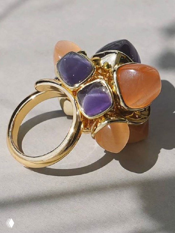 Крупный план золотого кольца с фиолетовыми и коралловыми вставками на светлом фоне, демонстрация текстуры металла и летнего дизайна