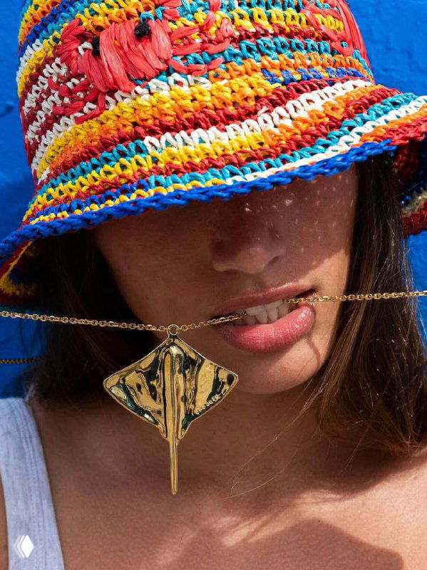 Модель в яркой вязаной панаме и подвеске с крупным декоративным элементом, кадр подчеркивает летний стиль и аксессуары