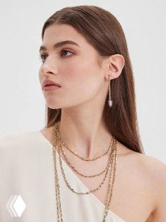 Боковой портрет молодой женщины с аккуратными серьгами и многослойными цепочками, минималистичная подача украшений на нейтральном фоне