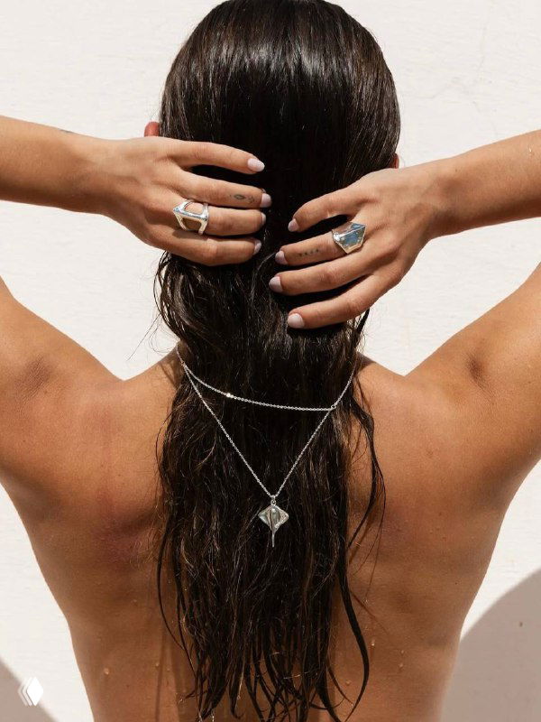 Вид сзади: женщина с длинными волосами носит несколько колец и подвесок, композиция подчёркивает летнюю атмосферу и аксессуары для пляжа