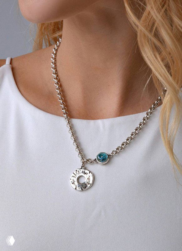Колье Ciclon серии Disfrutar на шее модели: цепочка с медальоном и бирюзовой вставкой, показ украшения на модели в светлом наряде.