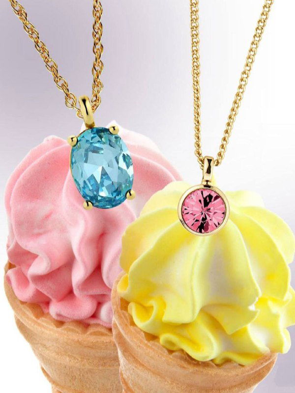 Две подвески Dyrberg Kern с голубым и розовым кристаллом на тонких цепочках, размещённые на декоративном фоне с мороженым в пастельных тонах.