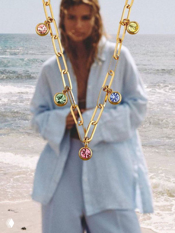 Цепочка Dyrberg Kern с небольшими подвесами-камнями разных цветов на размытом фоне моря и модели — визуал коллекции мульти цветов для лета.