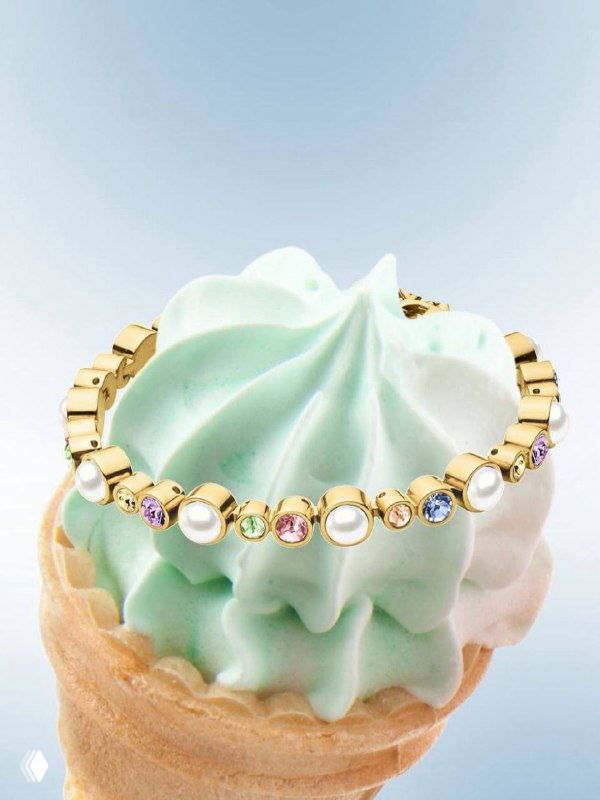Браслет Dyrberg Kern со множеством мелких разноцветных кристаллов на золотой основе, уложенный на пастельное мороженое как стилизованный реквизит для каталога.