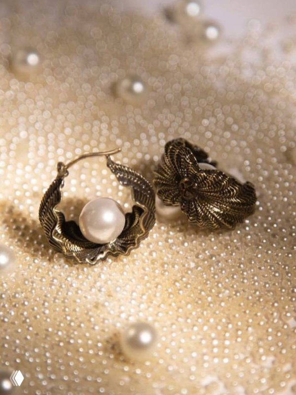 Крупный план парных серег-колец с крупным жемчужным жемчугом на золотистом текстурированном фоне, демонстрация деталей и отделки украшения.