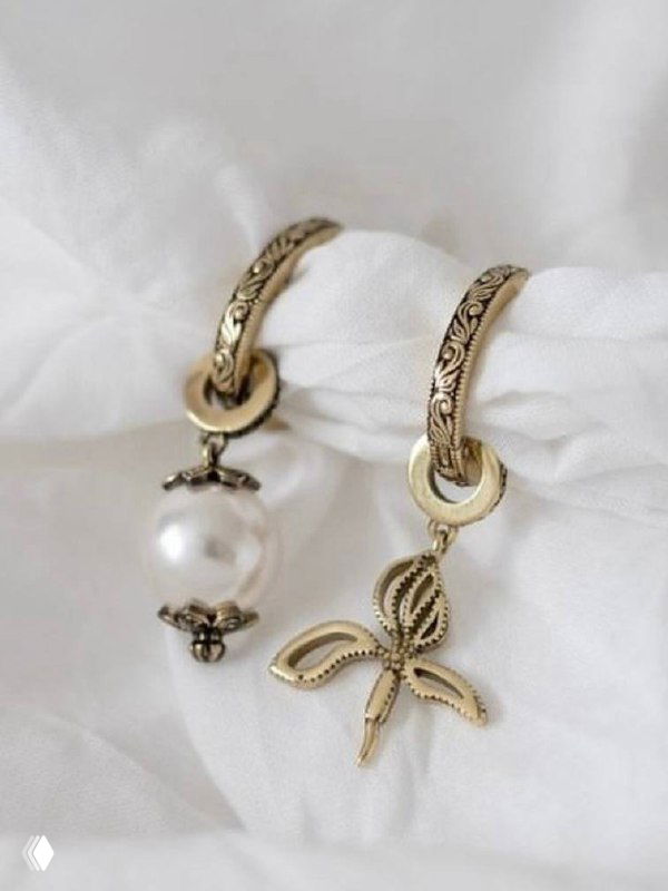 Детальный кадр подвесных серег с крупными круглымі жемчужинами и декоративными элементами на белой мягкой ткани, подчёркивающий текстуру и форму украшения.