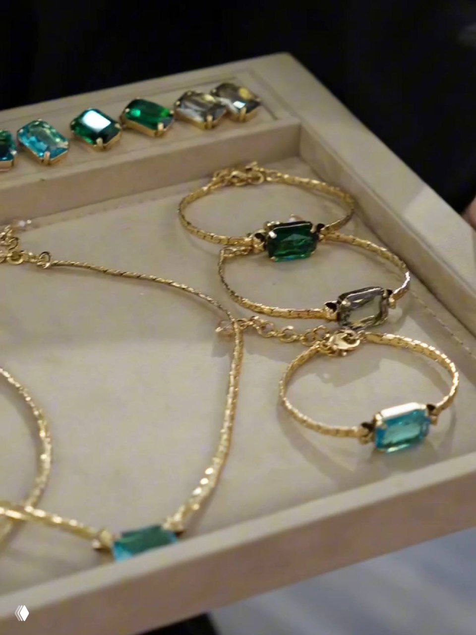 Детальный кадр коллекции Claudio Canzian: золотистые браслеты и колье с крупными прямоугольными зелёными и бирюзовыми кристаллами на подставке.