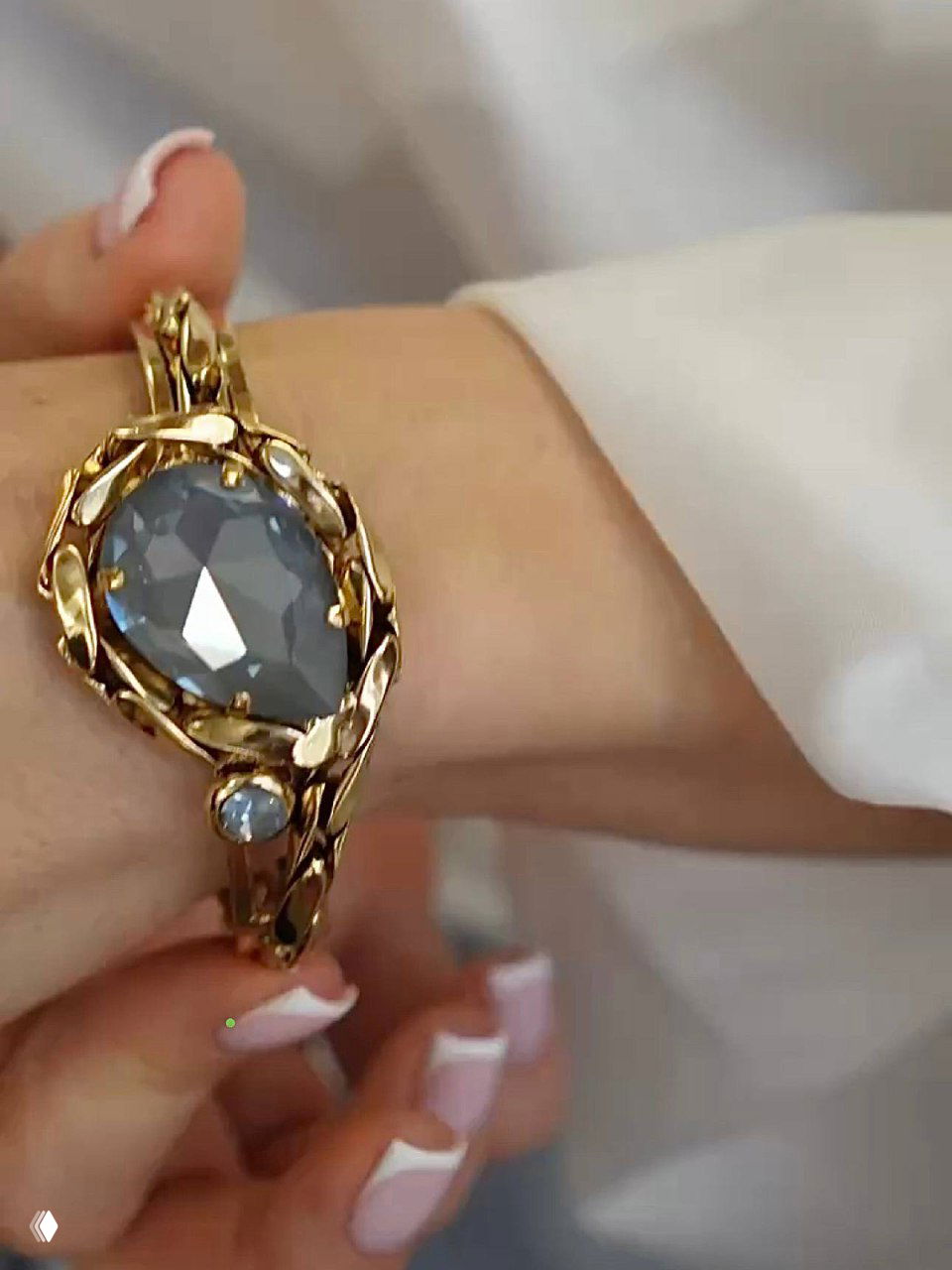 Крупный план браслета Claudio Canzian на запястье модели: крупный серо-голубой кристалл в декоративной золотистой оправе и плетёной основе.