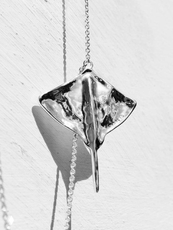 Чёрно-белый крупный кадр серебряной подвески в форме ската на цепочке, детальная текстура металла и минималистичный фон.