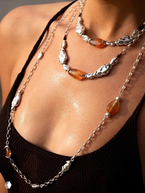 Крупный план ожерелья Liquid Ciclon: муранское стекло и серебристые элементы на загорелой коже, блеск и текстура украшения.