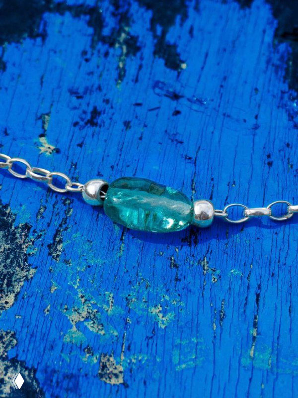 Макро-съёмка синей муранской бусины на тонкой цепочке из коллекции Liquid Ciclon на фактурном синем фоне.